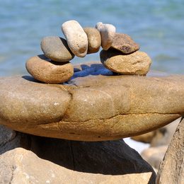 Équilibre Sculpture de pierres empilées en arc sur un rocher, en bord de mer.